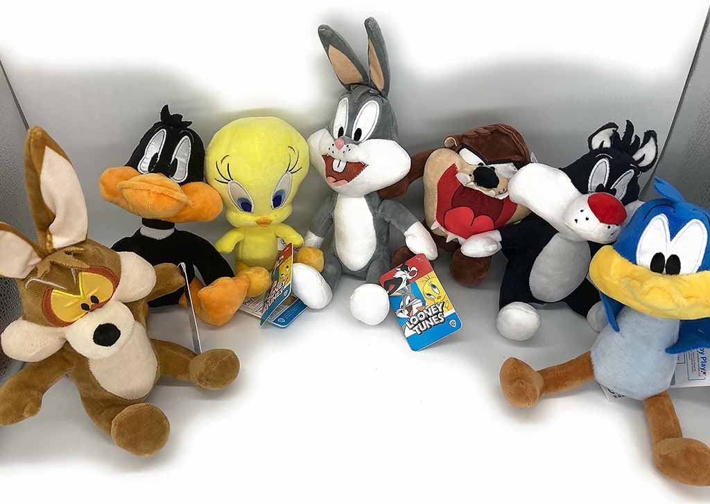 A lineup of Looney Tunes plush toys, including Wile E. Coyote, Daffy Duck, Tweety Bird, Bugs Bunny, Taz, Sylvester, and Road Runner, displayed together on a white background with their tags attached.