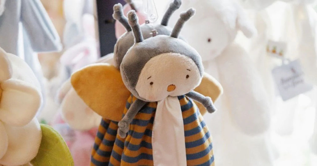 Cute bee-themed plush toy with soft wings and striped body hanging in a baby toy display.