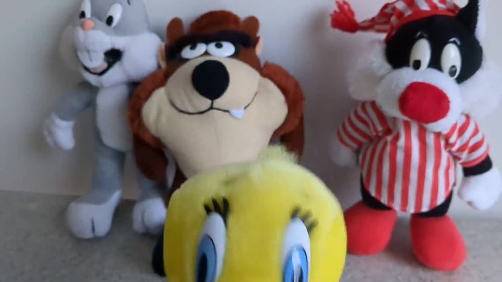 A group of cartoon-style plush toys standing together, including a gray rabbit, a brown character with big teeth, a black-and-white cat in red striped pajamas, and a yellow plush toy in the front with large blue eyes.