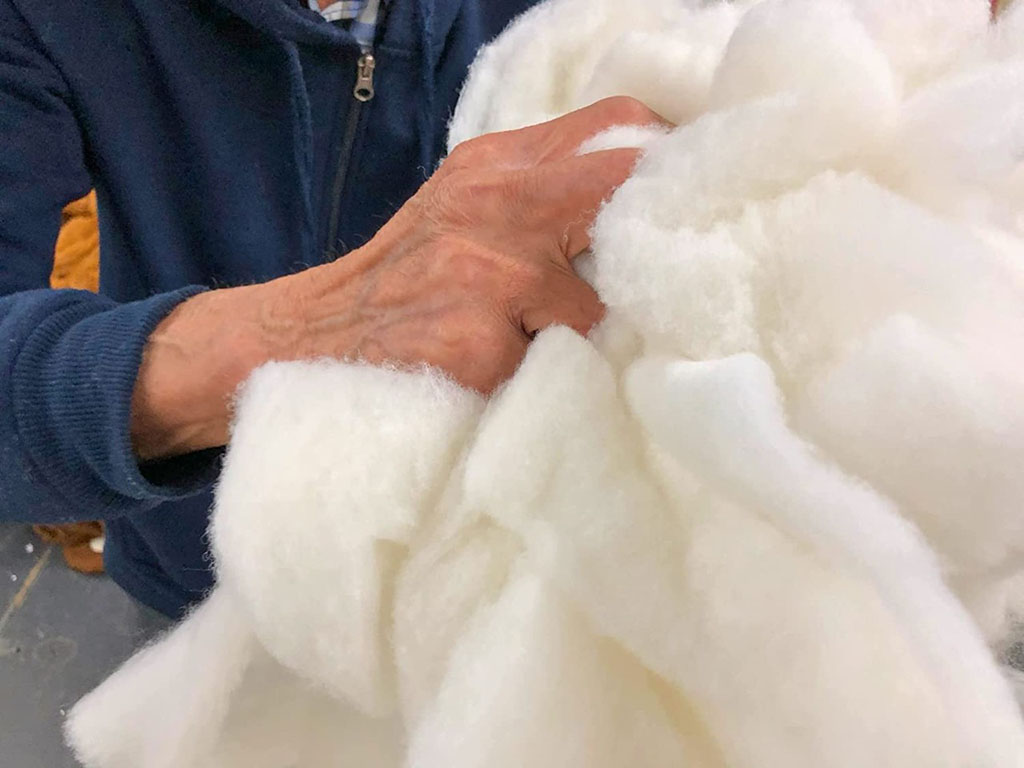 A close-up of a person holding a large bundle of soft white polyester fiberfill stuffing, commonly used in plush toy manufacturing for creating volume, softness, and shape.