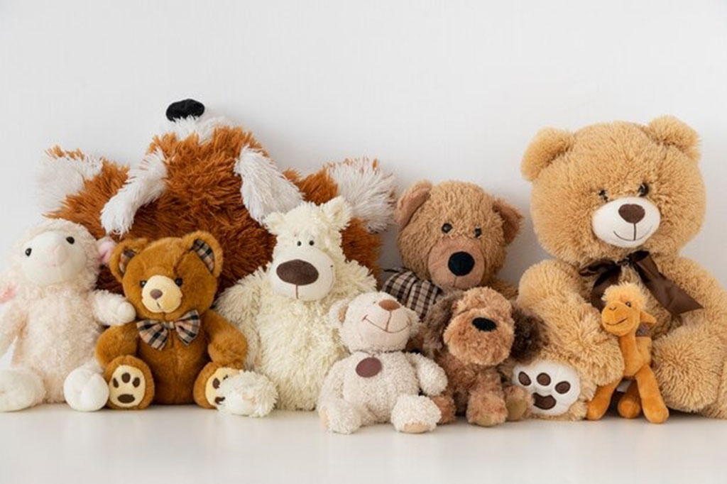 A collection of soft stuffed animals including teddy bears, dogs, and other plush toys arranged together against a white background.