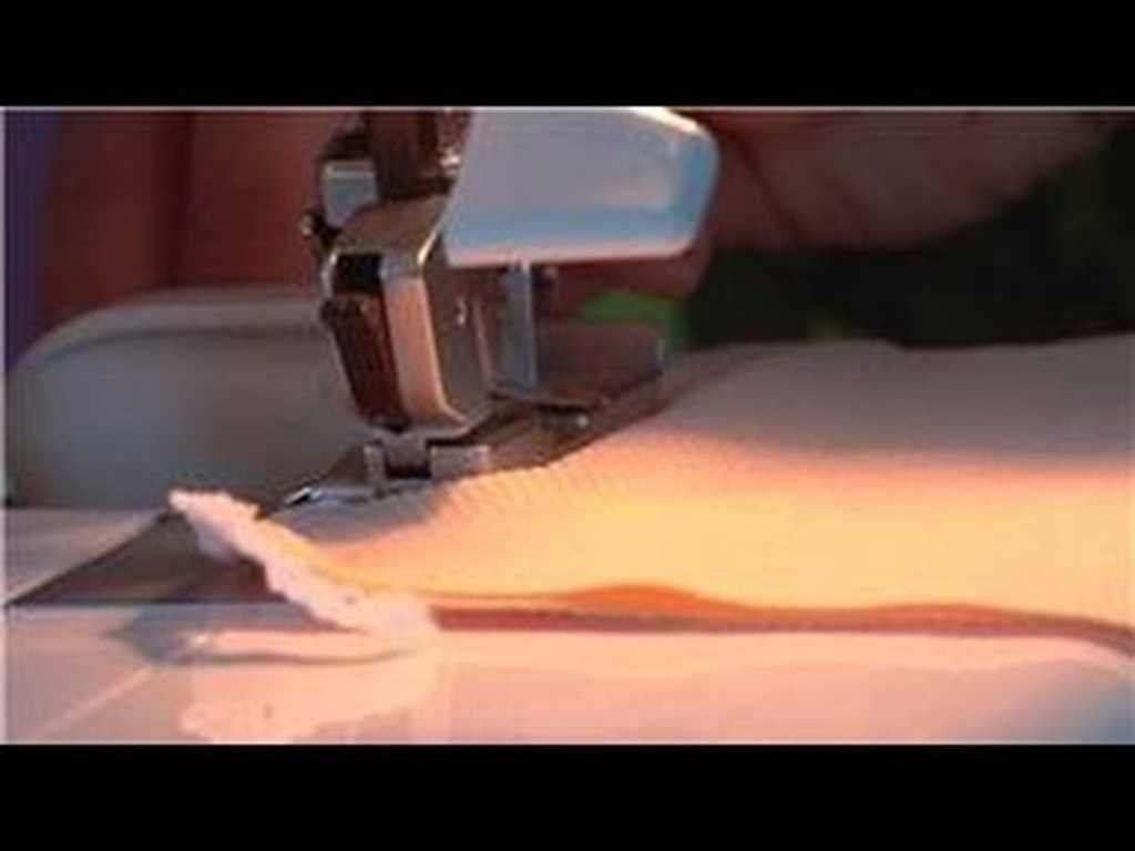 A close-up view of a sewing machine stitching light-colored fabric with a person guiding the material.