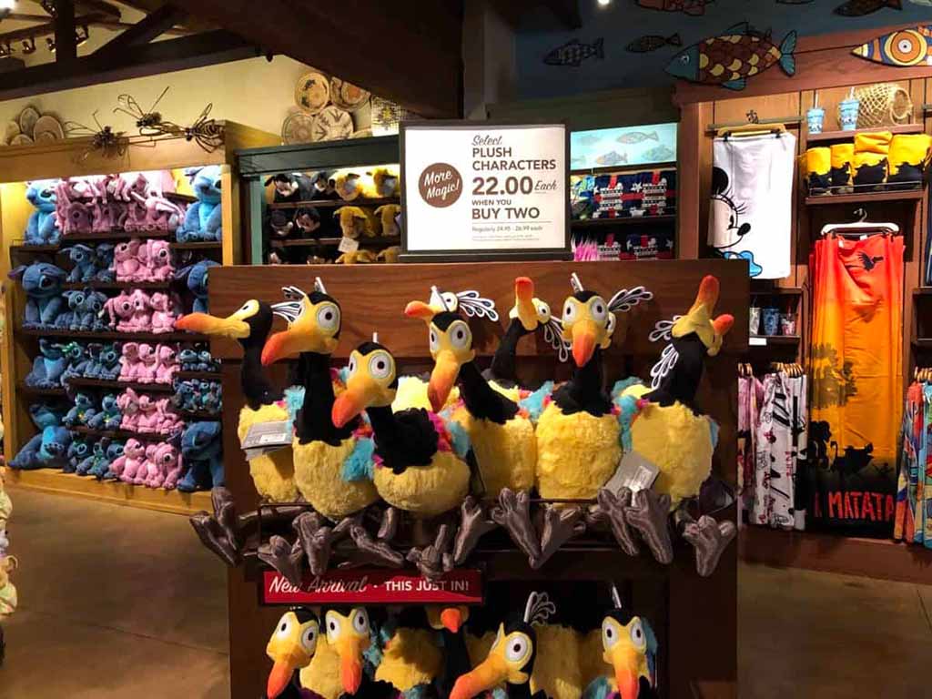 Colorful Disney plush toys, including Kevin bird characters from “Up,” displayed on wooden shelves in a themed retail store.