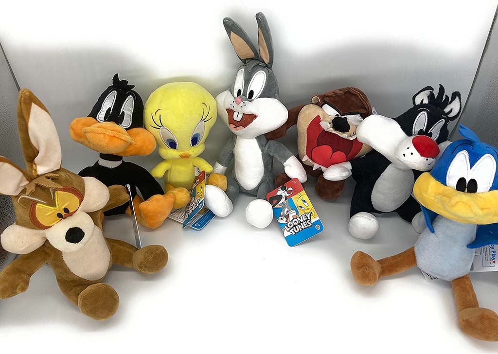 A group of six soft BumBumz plush toys in various fun designs including a flower, alien, peace sign, rocket, rainbow, and yin-yang character, displayed on a dark background.
