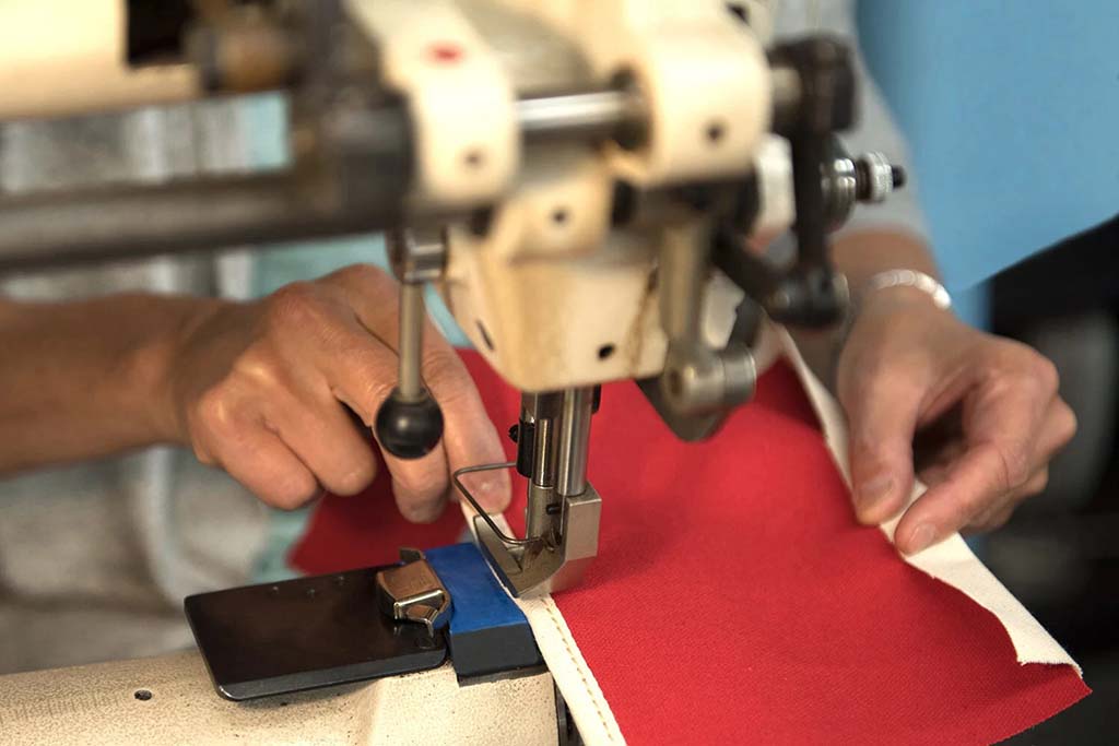 Close-up of hands guiding red fabric through an industrial sewing machine, showing precise stitching work during textile or plush toy production.