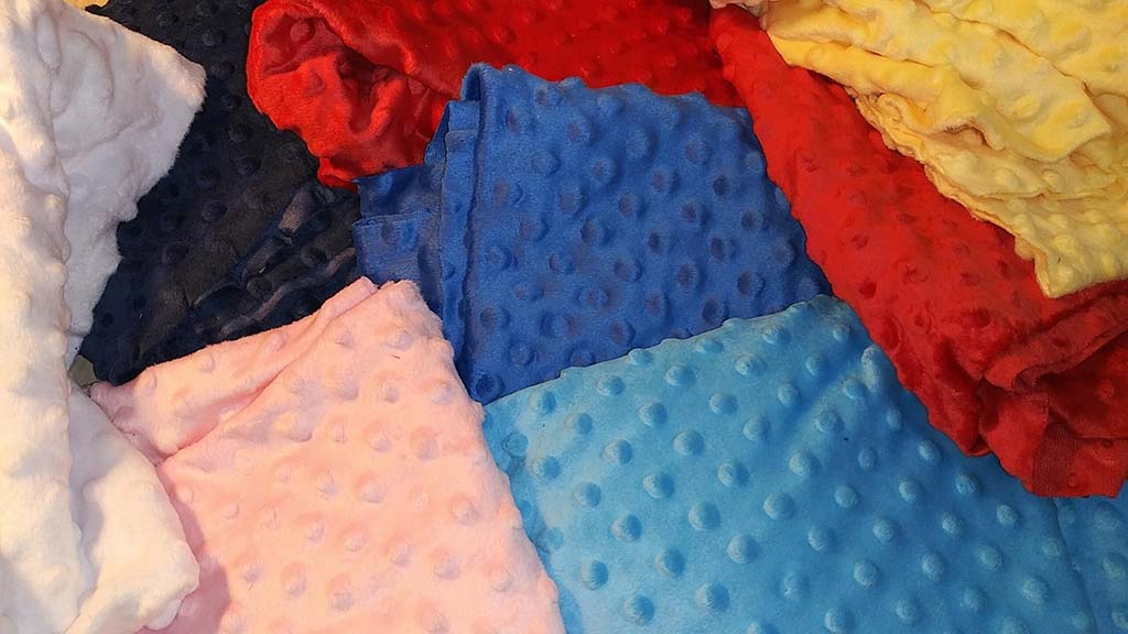 Various soft minky dot fabrics in red, blue, yellow, pink, white, and navy colors arranged together, showing plush texture and raised dot patterns.
