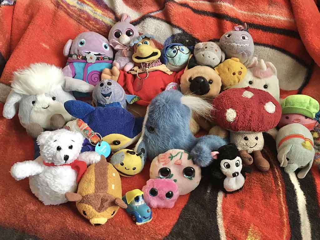 A colorful group of various small plush toys including animals, cartoon characters, and fantasy creatures displayed on an orange blanket.