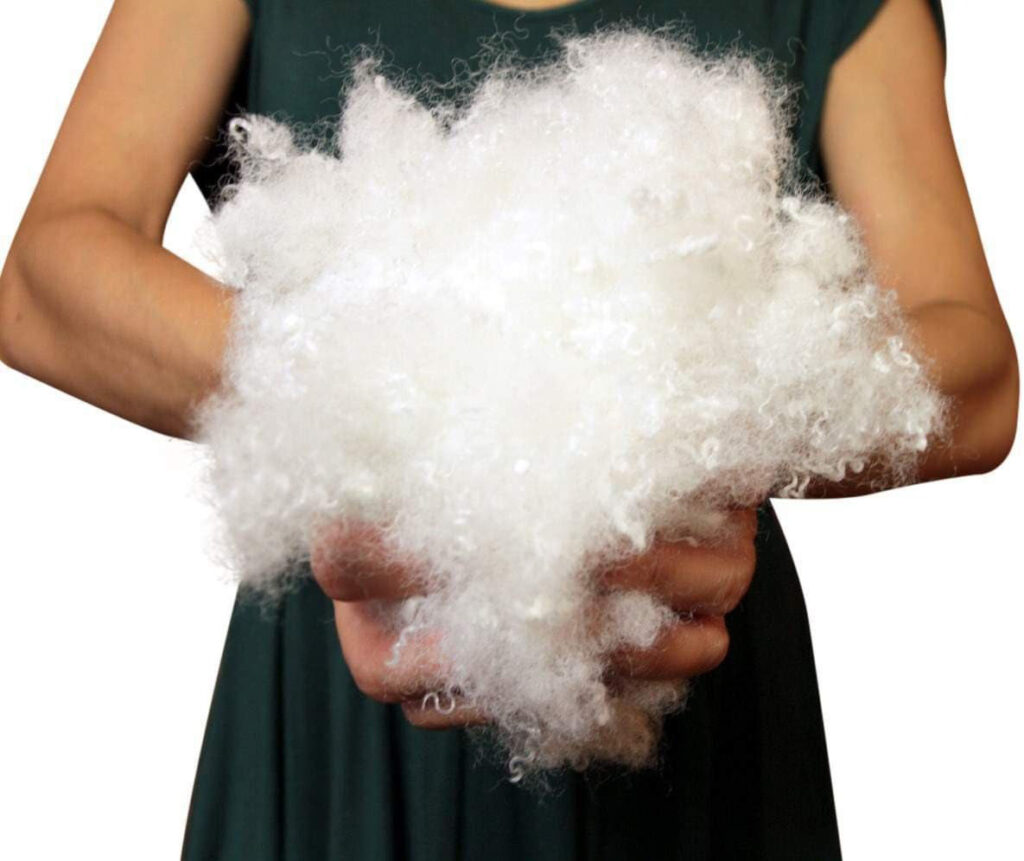 A person holding a large bundle of soft white polyester stuffing material used for filling plush toys.