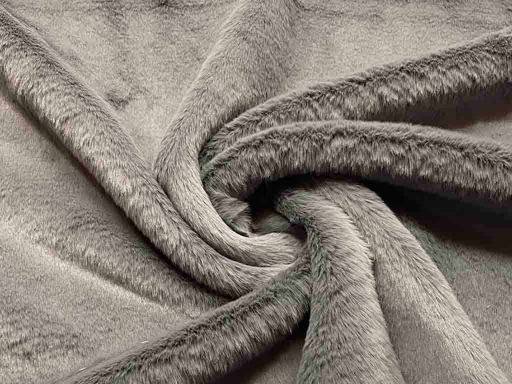 Close-up of soft grey faux fur fabric with long, dense fibers shown in folds, highlighting texture and plush quality for stuffed animal or textile use.