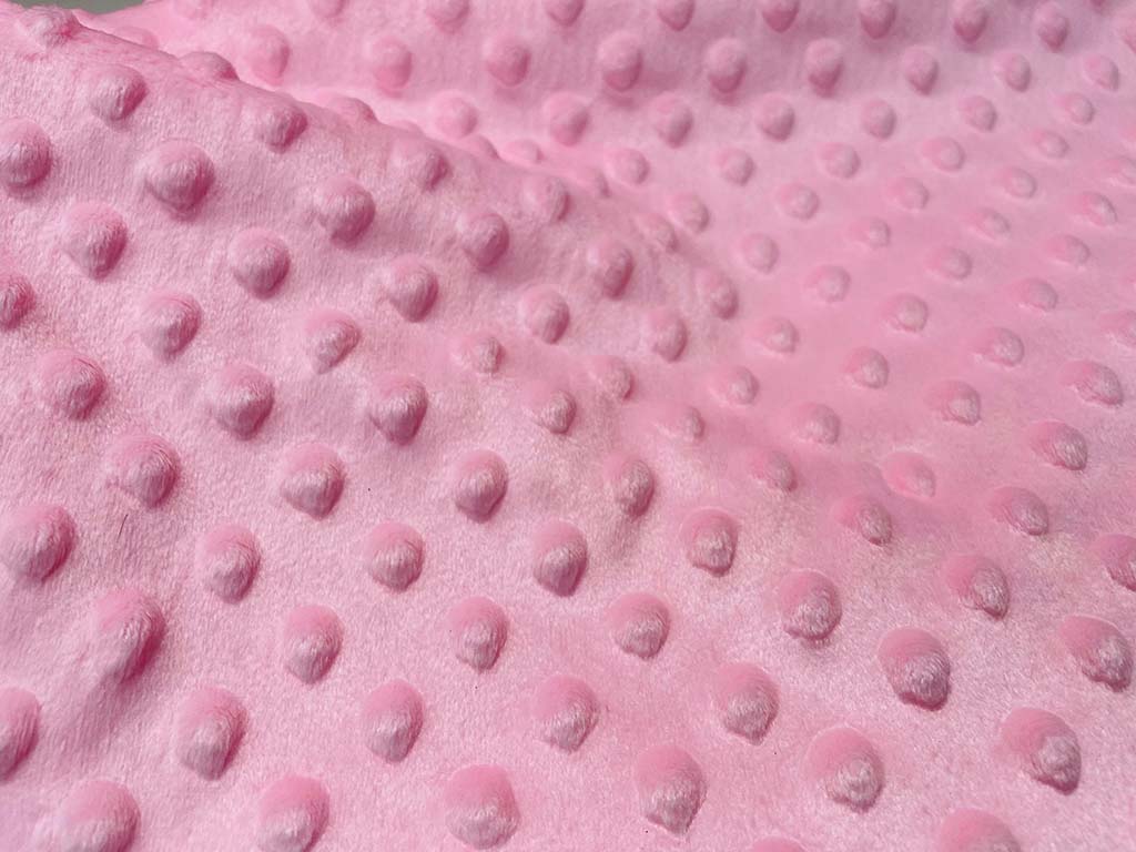 Close-up of soft pink minky dot fabric featuring raised textured bumps, commonly used for plush toys, baby blankets, and stuffed animal manufacturing.