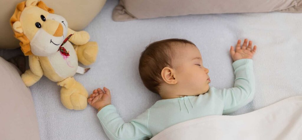 Baby sleeping peacefully on a bed with a soft plush lion toy resting beside them.