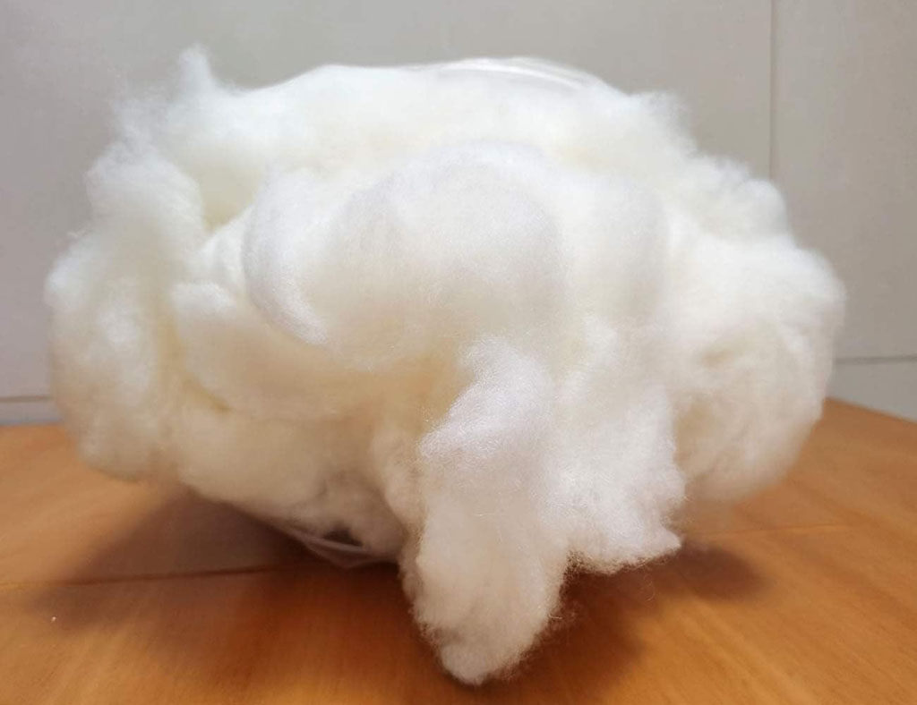 Soft and fluffy natural wool fiber placed on a wooden surface, commonly used as eco-friendly stuffing for plush toys and handmade cushions.