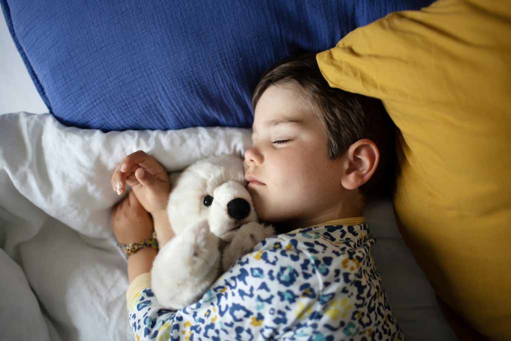 Young child sleeping peacefully while hugging a soft stuffed animal in bed with pillows.