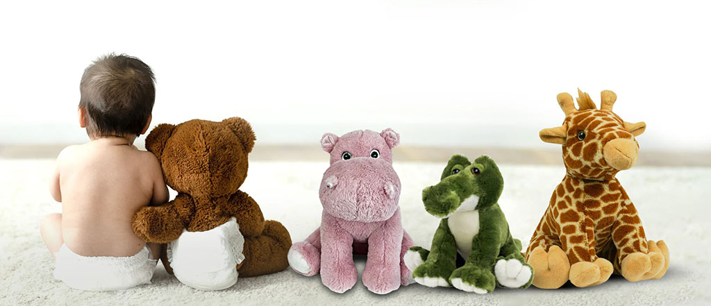Baby sitting with a brown teddy bear, facing a row of plush animals including a pink hippo, green crocodile, and giraffe on a light floor.