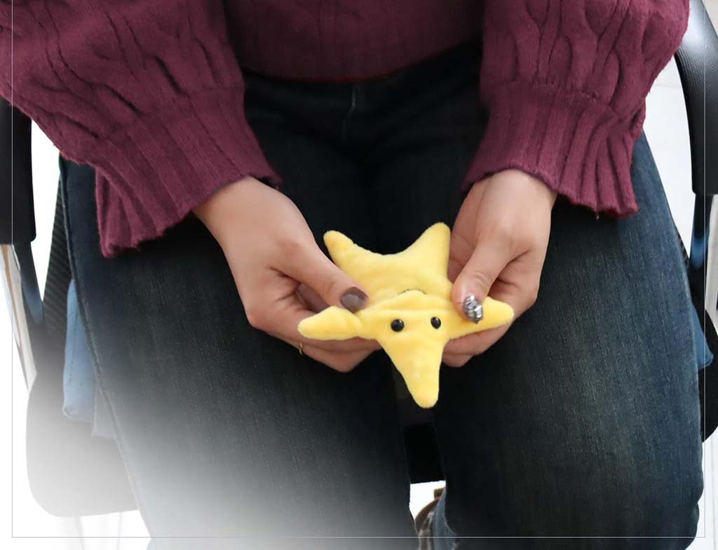 Person holding a small yellow star-shaped plush toy in their hands, demonstrating compact size and soft, squeezable texture.