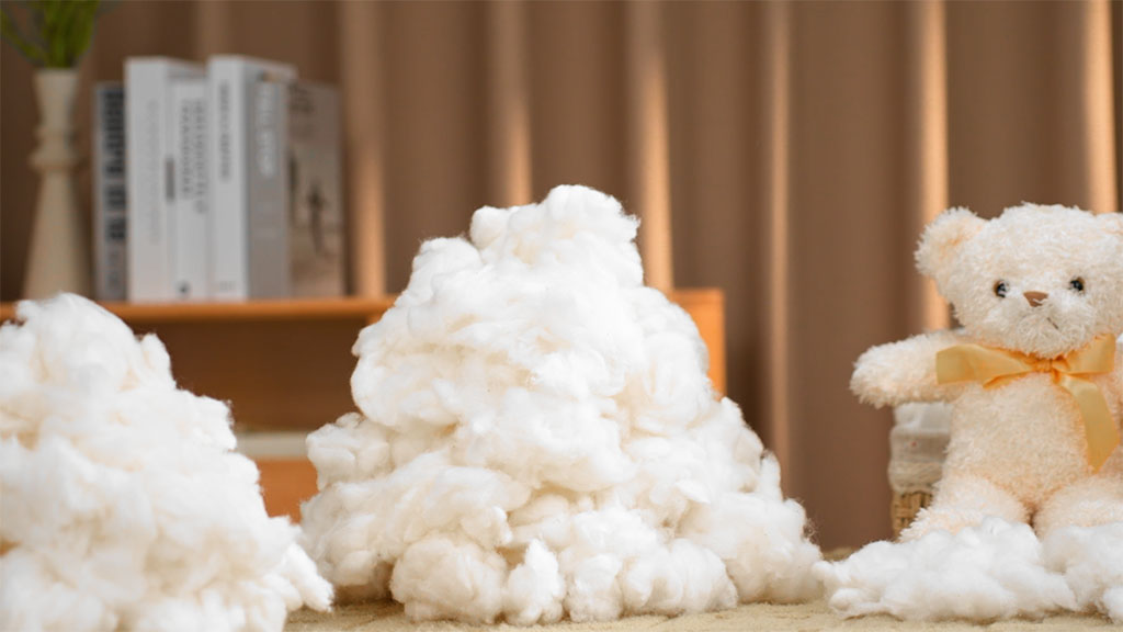 Piles of plush toy fiber filling displayed beside a finished teddy bear, showing stuffing material used in soft toy manufacturing.