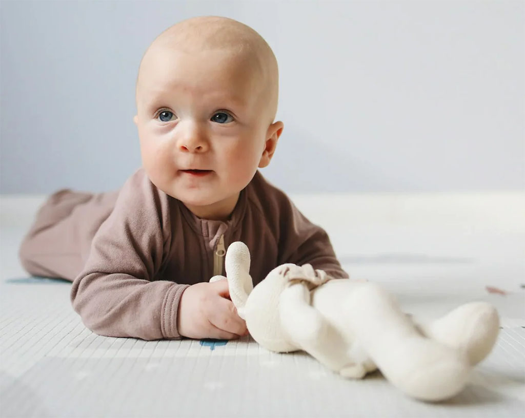 Baby lying on a soft mat, holding a small plush toy while looking forward.