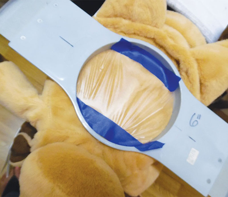 Close-up of a plush toy body secured in a large embroidery hoop, with masking tape holding soft yellow fabric in place for machine embroidery
