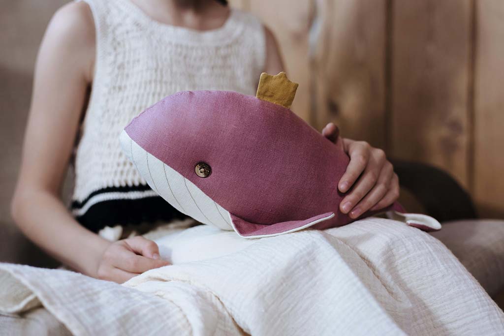 A child sitting indoors while gently holding a handmade whale-shaped plush toy, showing comfort and emotional attachment.