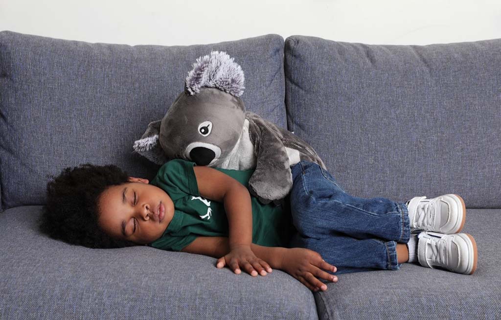 A toddler peacefully sleeping on a sofa while cuddling a soft weighted plush toy, conveying comfort, security, and relaxation.