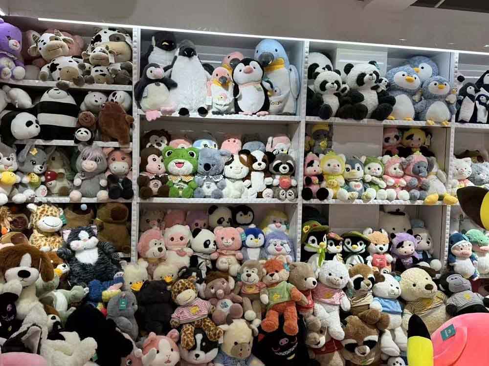 Large retail display shelves filled with assorted stuffed animals, including teddy bears, pandas, penguins, and other plush toys arranged tightly for bulk sale.