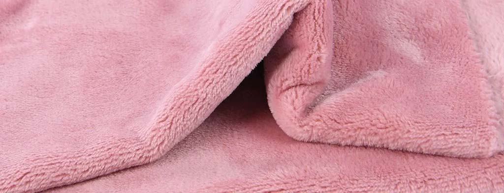 Pink fleece fabric close-up showing a smooth, dense pile and soft surface texture, commonly used for plush toys, blankets, and cozy stuffed animal exteriors.