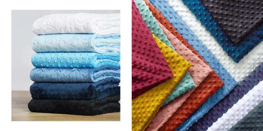 Stack of folded soft minky blankets in gradient blue, white, and black tones beside a spread of colorful dotted minky fabrics in multiple colors.