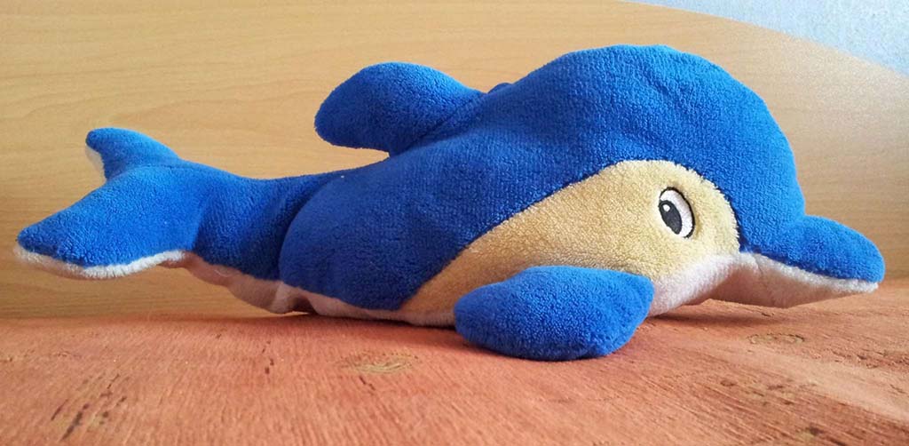 Hand holding a handmade fabric bunny doll wearing floral shorts, with embroidery thread and small scissors placed on a striped fabric background.