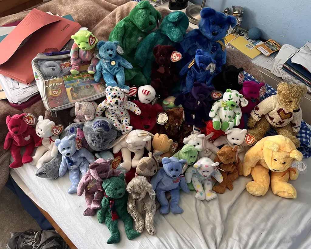 Large collection of vintage Beanie Babies plush toys arranged on a bed, featuring assorted teddy bears in various colors with TY heart-shaped tags.