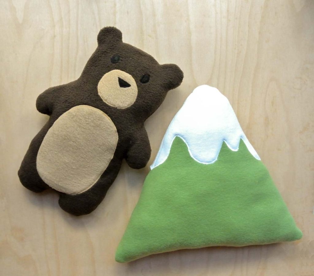 Handmade plush bear and soft mountain-shaped plush pillow made from fleece fabric, laid flat on a light wooden surface.