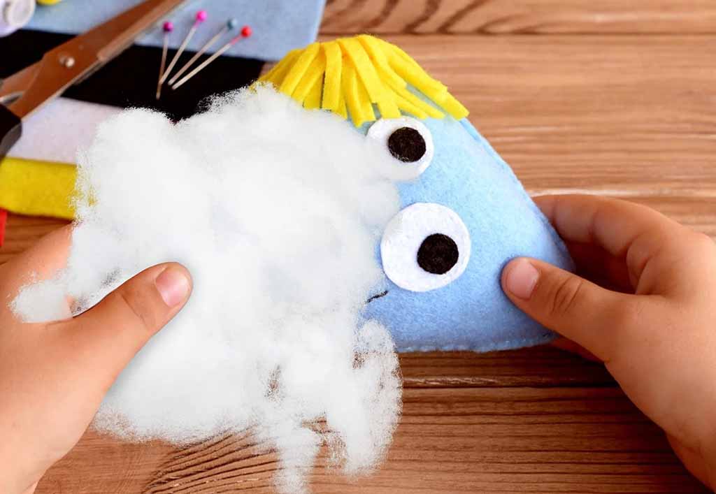 Hands stuffing white polyester fiberfill into a handmade felt plush toy during DIY soft toy sewing