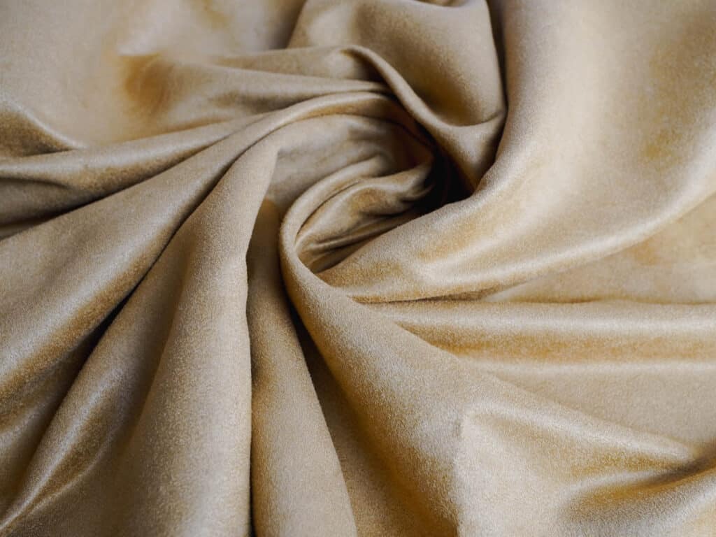 Close-up of beige faux suede fabric with soft, smooth texture, folded in gentle swirls to show drape and surface finish