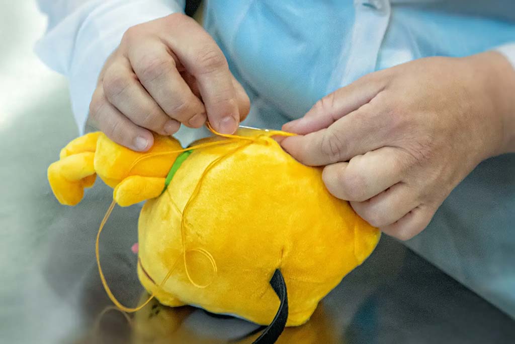 Factory worker hand-stitching a yellow plush toy body, closing the seam during soft toy manufacturing.