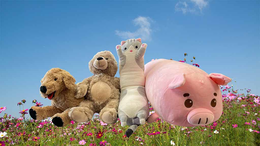 Four plush stuffed animals sitting together on a wooden fence in a colorful flower field under a clear blue sky, including a dog, teddy bear, cat, and pink pig plush, creating a cheerful outdoor scene.