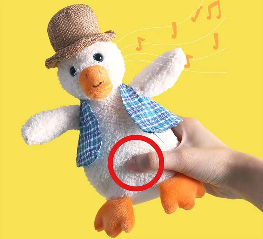 Squeeze-activated musical duck plush toy wearing a hat and vest, with a hand pressing the belly area highlighted to show the sound activation point.
