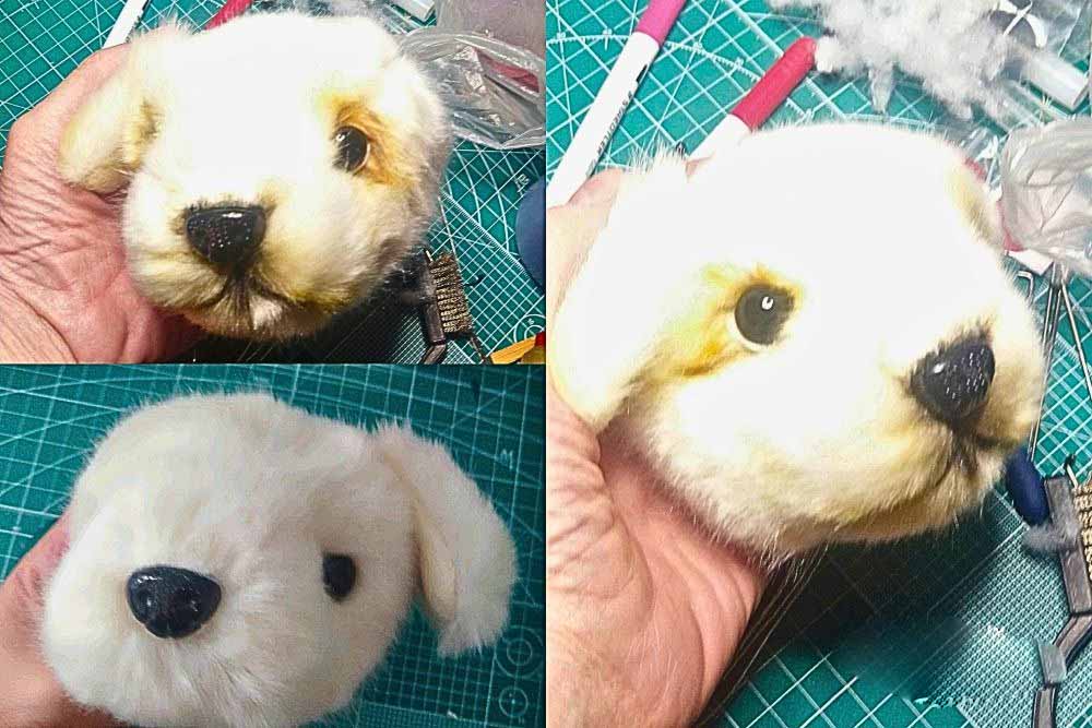 Handmade plush dog head in progress, showing detailed nose, eyes, and fur shaping on a crafting table with tools and stuffing materials.