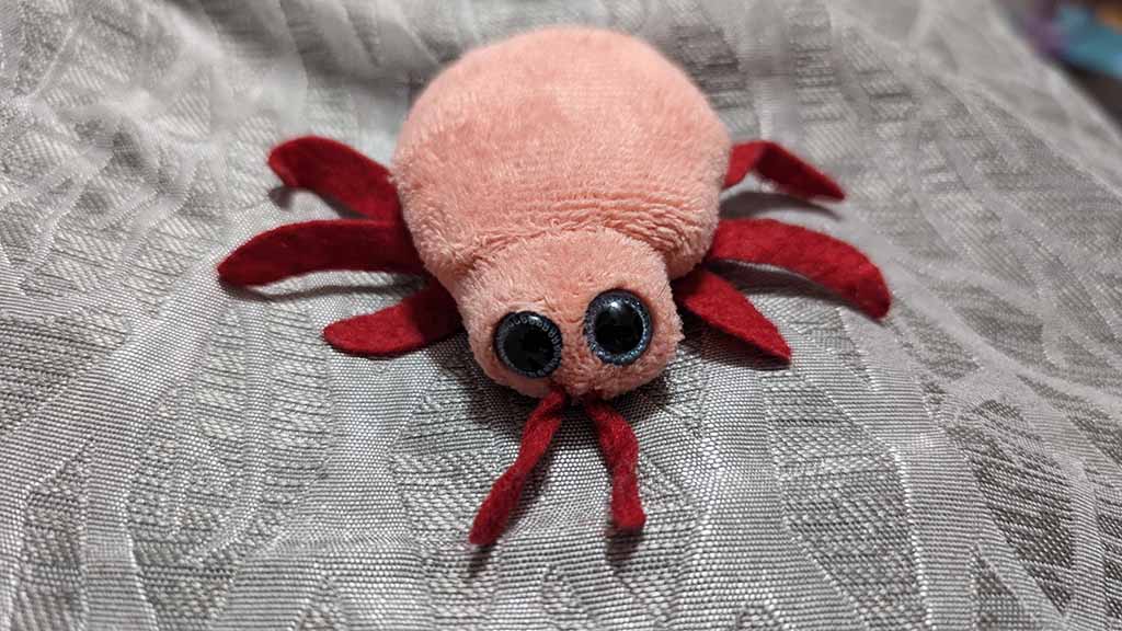 Small pink spider plush toy with big eyes lying on fabric
