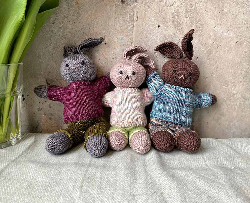 Three handmade knitted bunny plush toys sitting side by side, featuring soft yarn textures, simple embroidered facial details, and cozy knitted sweaters, designed as eco-friendly stuffed animals suitable for baby gifts, nursery decor, artisan plush collections, and custom plush toy design inspiration.