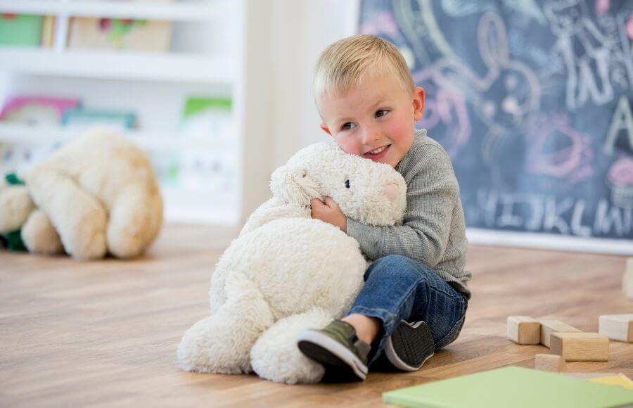 A young child sits on the floor of a playroom and hugs a large, fluffy white plush toy, showing how stuffed animals provide comfort, emotional security, and sensory support for kids.