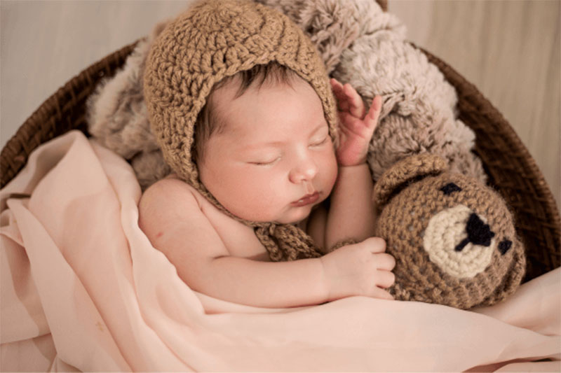 Newborn baby resting beside a soft stuffed animal in a styled, supervised setting, illustrating gentle textures and newborn-friendly plush design while avoiding any implication of unsupervised sleep or crib use.
