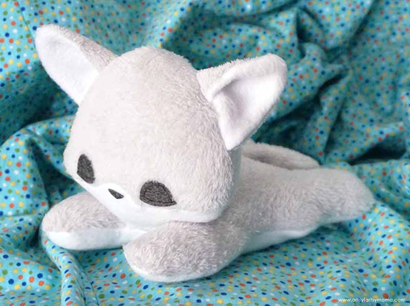 Soft white wolf plush toy lying on a patterned blue blanket, showcasing a gentle, cuddly design suitable for babies, toddlers, and comfort-focused plush collections.