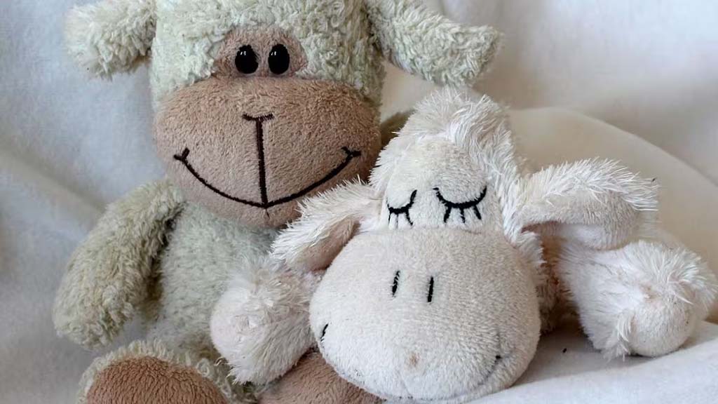 Two soft plush sheep toys sit cuddled together, one smiling and one appearing asleep, showcasing the comforting and calming appearance of well-loved stuffed animals.
