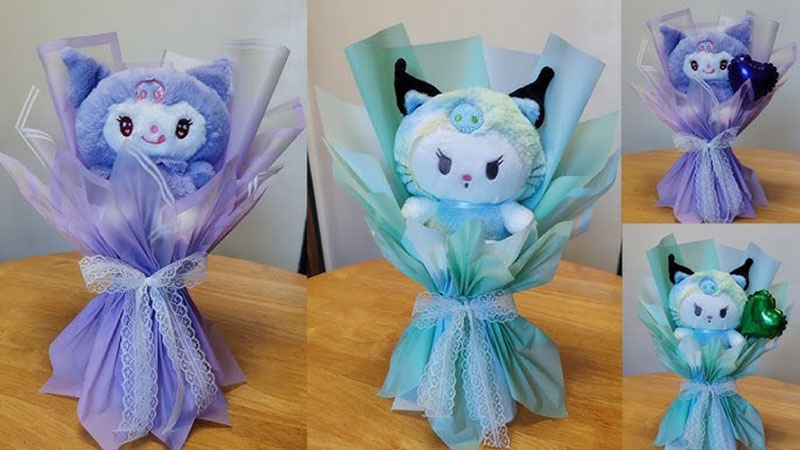 Multiple plush toy gift bouquets wrapped in layered pastel papers and lace ribbons, featuring cute blue and turquoise plush characters displayed on a wooden table.