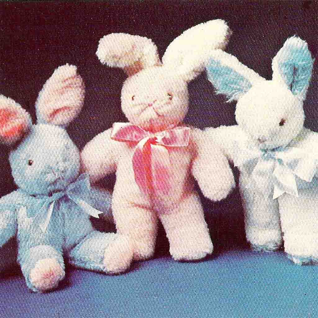 Three vintage-style stuffed bunny toys in blue, pink, and white, each with ribbon bows, posed against a dark background.
