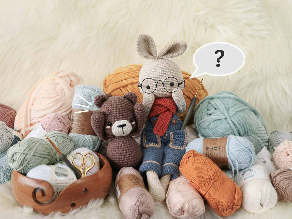 Handmade amigurumi crochet dolls surrounded by colorful yarn balls and knitting tools, featuring a bunny doll with glasses and a small bear, highlighting artisanal craftsmanship, soft texture materials, creative plush design inspiration, and handmade crochet toy concepts suitable for boutique plush brands and custom soft toy development.