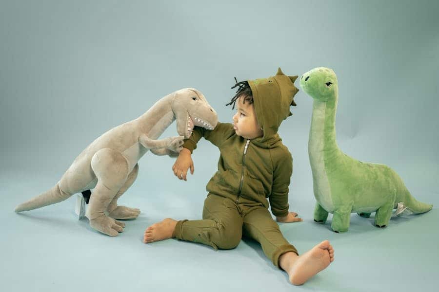 Child in dinosaur costume playing with plush dinosaur toys.