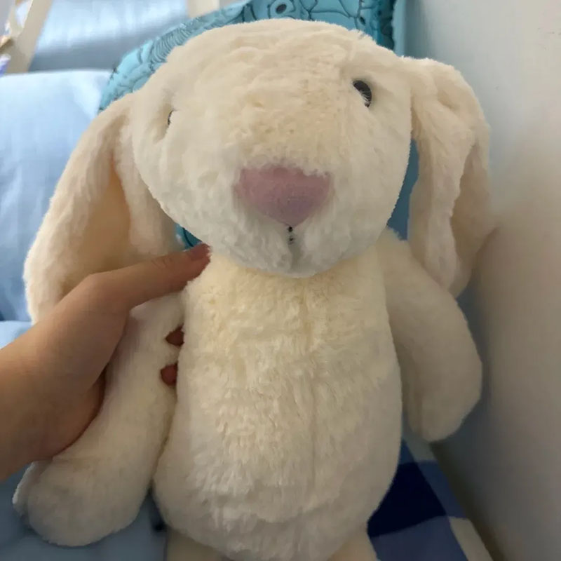 Soft white bunny plush toy with floppy ears being held by a hand.