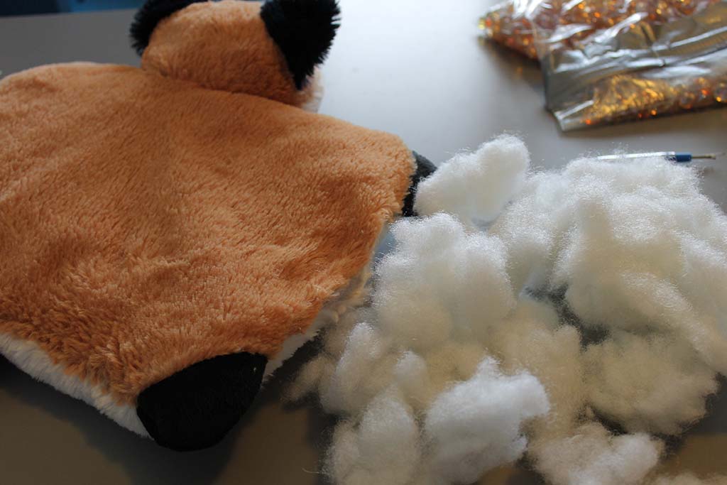 Close-up of a partially opened plush toy showing loose white polyester fiberfill stuffing used inside stuffed animals during manufacturing or repair.