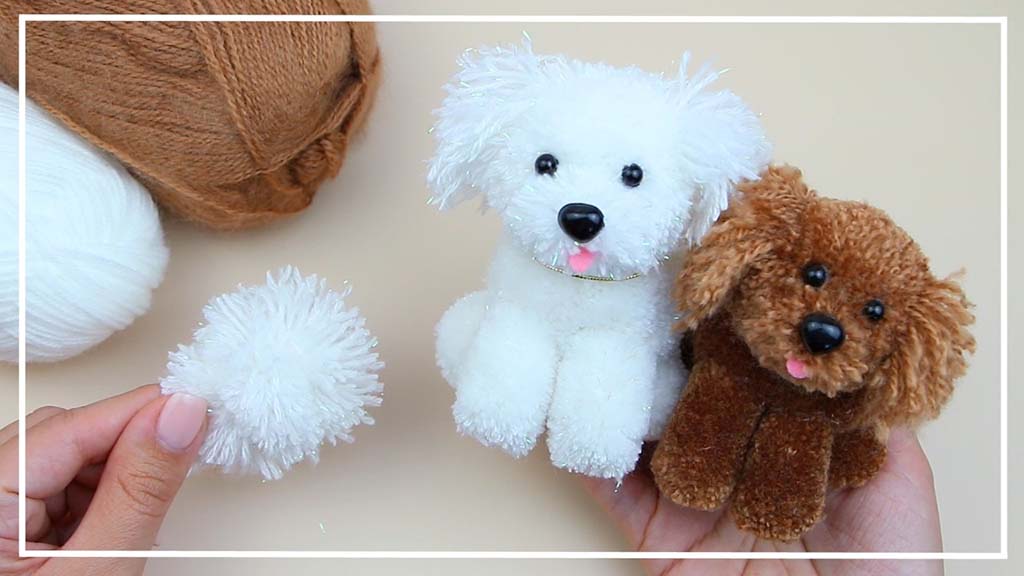 Two handmade pom-pom puppies, one white and one brown, shown with yarn balls and a small white pom-pom during a DIY craft process.