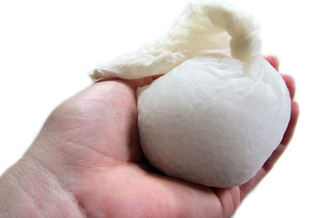 A close-up of a hand holding a small white fabric pouch filled with poly pellets, commonly used as weighted stuffing material for plush toys, dolls, and sensory items.